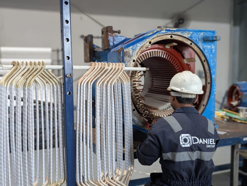 Technician from Daniel Group working on the stator of a large industrial electric motor inside a workshop environment.
