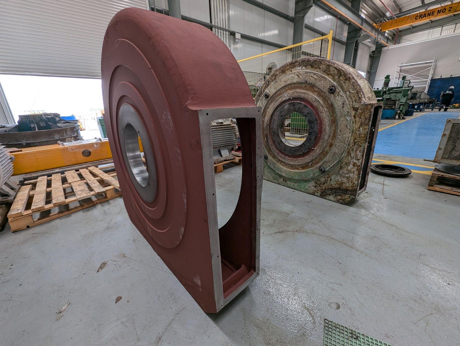 Fabricated industrial equipment casing in red primer on the workshop floor beside a used casing